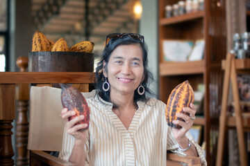 Asian middle-aged woman holds tropical fruit holding, cocoa fruits, in local cafe and drinks shop.