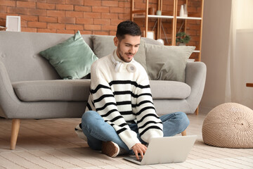 Obraz premium Handsome young happy man with laptop resting on floor at home