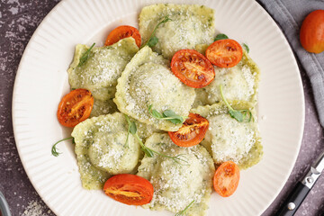 Plate of tasty ravioli with tomatoes and cheese on grey background