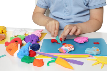 Naklejka premium Little boy sculpting with play dough at table on white background, closeup