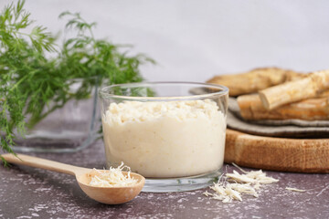 Horseradish sauce in bowl and spoon with ground horseradish on grey background