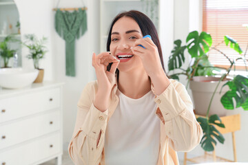 Beautiful young happy woman with dental floss in bathroom at home