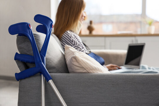 Crutches of injured woman after accident using laptop at home, closeup