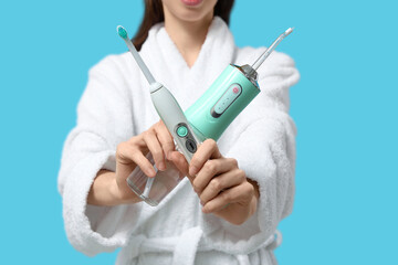 Young woman with oral irrigator and electric toothbrush on blue background