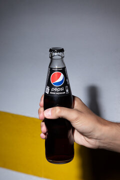 A close-up shot of a hand holding a bottle of Pepsi Zero Sugar against a grey and yellow background. The image highlights the branding and emphasizes the refreshing nature of the sugar-free beverage.
