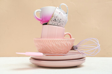 Clean cups, plates and whisk on table against beige background