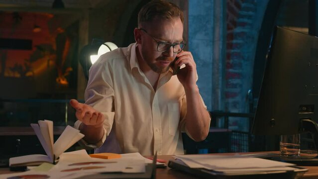 Stressed tired angry aggressive furious business man at night office overworked talking mobile phone call arguing conflict quarrel talk problem businessman male guy paperwork late time overtime stress