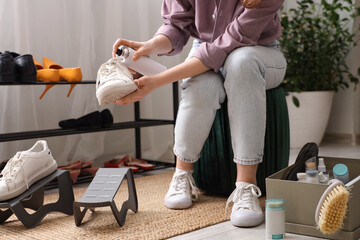 Woman applying water repellent spray on stylish sneakers at home