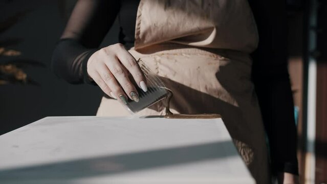 Brown, thick and viscous resin is poured onto the canvas in the artist's studio, marking the beginning of the creation process for a resin painting. Close up. Slow motion