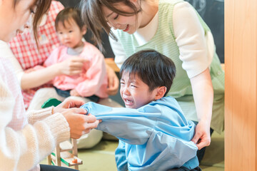 Obraz premium 保育園・幼稚園でお着替えをする保育士の女性とぐずるイヤイヤ期の園児の男の子 