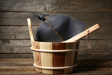 Bucket with ladle and felt hat for sauna on wooden background
