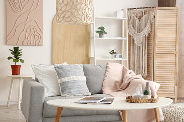 Light interior of stylish living room with sofa, pillows, shelving unit and coffee table