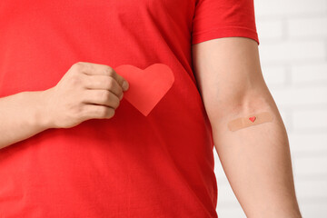Blood donor with applied medical patch and paper heart in clinic