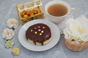 A cup of tea and a donut on a plate, a delightful combination for a relaxing break.
