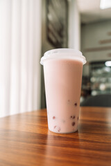 Chocolate bubble tea in plastic glass with lid on wooden table.