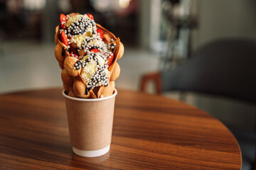 Bubble waffles in a cup with ice cream and strawberries on a wooden table.