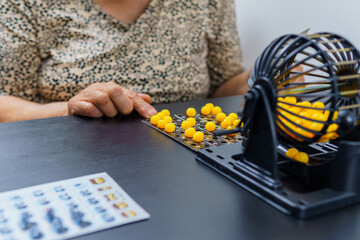 an elderly person who is playing bingo, he has a board of organized ballots and a ballot box