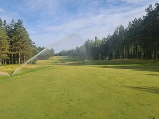 Obraz premium Sprinkler System Watering Golf Course Green on Sunny Day