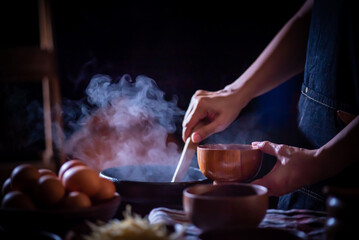 A porridge shop at night on the side of the road as the cook uses a wooden ladle to scoop porridge into a wooden bowl in a retro style. There were eggs and sliced ​​ginger placed on the table.