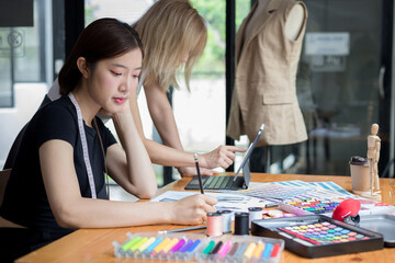 Fototapeta premium Young team asian designer women working at studio. Dressmaker makes clothes job