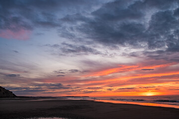 Captured at dusk, this image showcases a beautiful sunset over an expansive beach with colorful skies.