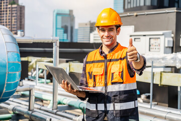 Portrait of caucasian engineer man in uniform holding laptop computer and working in at plumbing and electrical systems on the roof of a building, look at camera with cheerful smiles