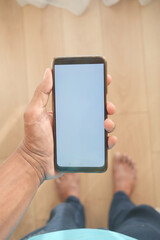 A hand is holding a smartphone with a blank screen on a wooden floor in a closeup shot