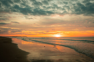 Serene beach scene at sunset with stunning orange and pink hues, reflecting on wet sand and gentle waves.