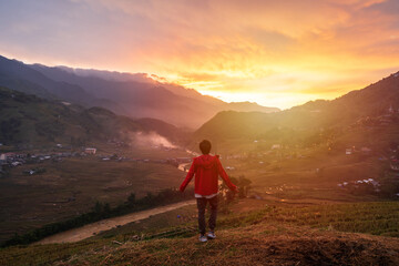 Obraz premium Young man traveler looking at beautiful landscape with mountains and green rice terraces view at sunset in Sapa, Vietnam