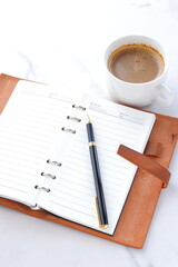 ミルクをたっぷり入れたコーヒーを飲みながら、茶色の革のシステム手帳を開いてデスクワーク中のイメージ
