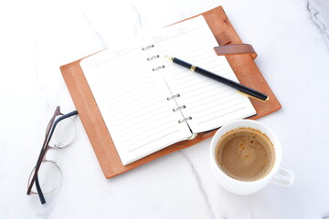 ミルクをたっぷり入れたコーヒーを飲みながら、茶色の革のシステム手帳を開いてデスクワーク中のイメージ
