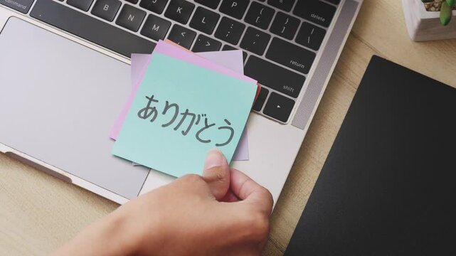 A Hand Put On colorful Paper Note With Text THANK YOU In Different Kind Of Languages On Laptop
