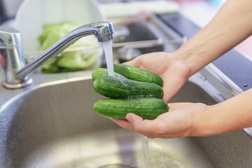 Woman hands washing fresh green baby cucumbers in kitchen