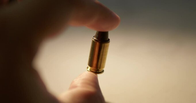 A close-up shot of an individual holding a single bullet between his thumb and forefinger.