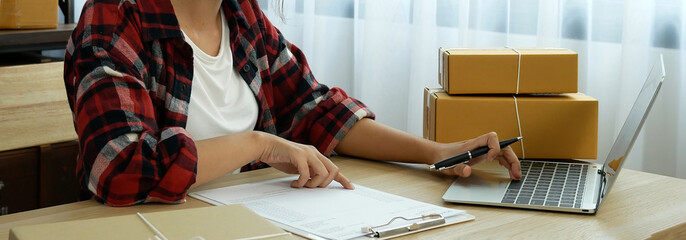 Banner Online seller Close up hands Young asian woman typing laptop keyboard checking online order on stock delivery package. Asian woman startup small business at home office with copy space