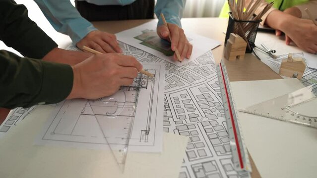 Smart architect and safety engineer discussion about building blueprint on table with architectural document, measurement tools and wooden block scatter around at modern office. Closeup. Delineation.