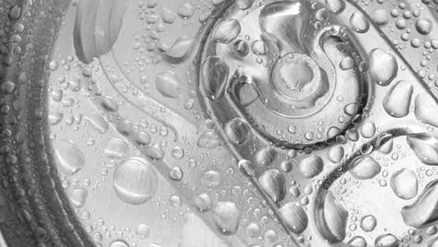 Close-up reveals water droplets adorning the aluminum can, highlighting the tactile ridges and prominent pull tab. Every droplet a testament to the condensation's delicate dance. Metallic  background.