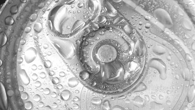 Zoom in, a beverage can's crown is a mesmerizing canvas of shimmering droplets, each enhancing the cool, crisp vibe of the metal surface, inviting a sip of refreshment. Metallic  background.
