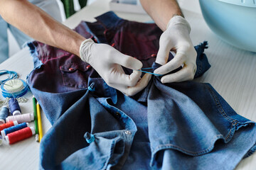 A young tailor meticulously sews a denim garment in his atelier, committed to reviving discarded...