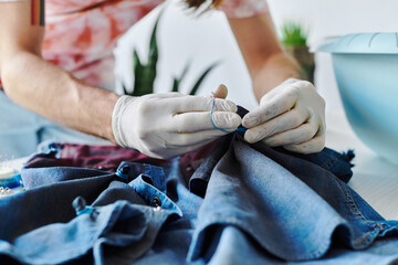 A young designer sews denim fabric in his atelier, focusing on sustainability by giving old...