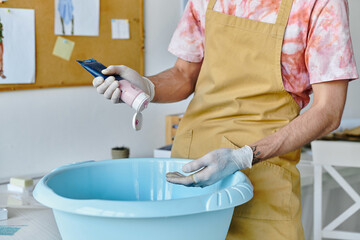 A young man in an apron and gloves prepares to dye fabric in his clothing restoration atelier.