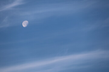 Daytime moon shines in clear blue sky with light clouds, creating serene atmosphere in nature