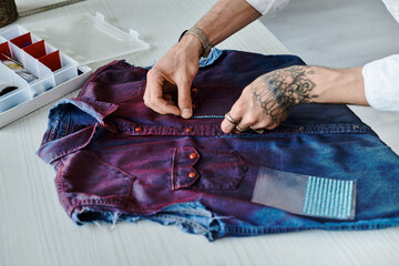 A young man with tattoos works on a discarded denim shirt, giving it new life with sustainable...