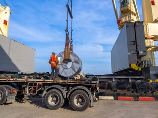 Loading of hot rolled steel coils on board of cargo ship using braided wire slings and heavy crane.