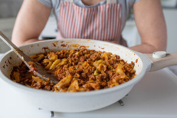 Woman with apron serving a fresh cooked homemade meal with minced meat, cabbage and vegetables in a frying pan