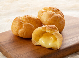 Cream puffs on a cutting board placed on a cloth background.