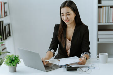 Asian Businesswoman Using laptop computer and working at office with calculator document on desk, doing planning analyzing the financial report,