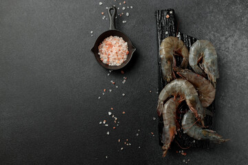 Large king prawns raw on a black cutting board. Hot pepper, salt. Black background