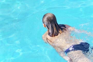 unrecognizable woman swimming in a pool without swimsuit top