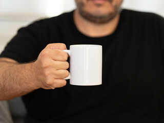 A man in a black t-shirt with a blank coffee mug holding in hand. Best for PSD mockup and representing your branding. It's a perfect white mug position.